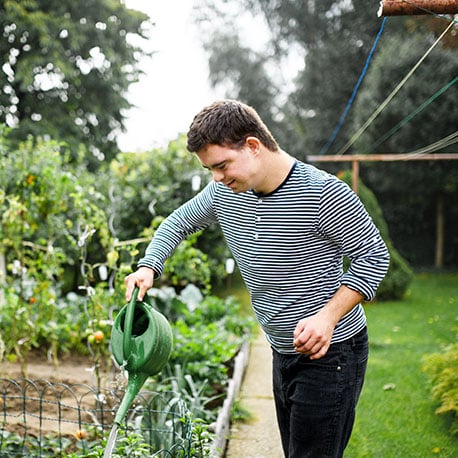 Young man watering plants at his new home he bought with a first time homebuyer savings account