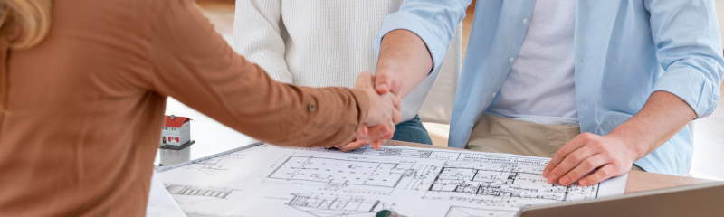 young couple shaking hands with realtor over new house blueprints