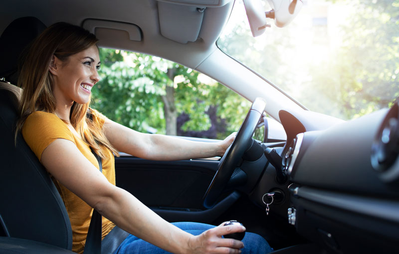 Woman-driving-home-the-best-used-car-for-her-lifestyle-and-budget-while-smiling-behind-the-wheel-in-a-yellow-shirt.