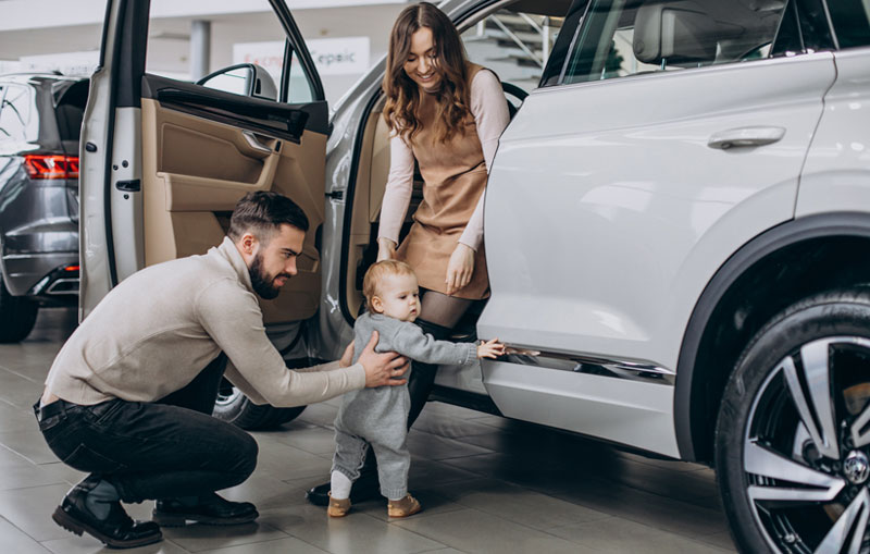 Young-family-with-baby-at-dealership-learned-the-best-time-to-buy-a-car-so-they-smile-with-their-new-car-payment-and-ride.